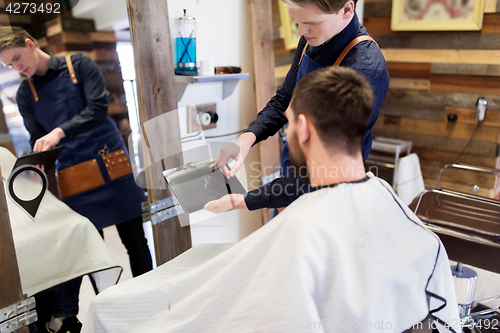 Image of barber showing tablet pc to man at barbershop