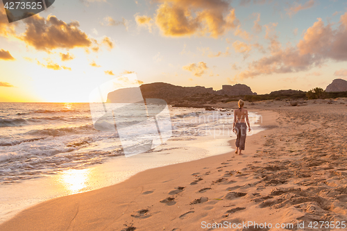 Image of Woman walking on sandy beach at sunset.