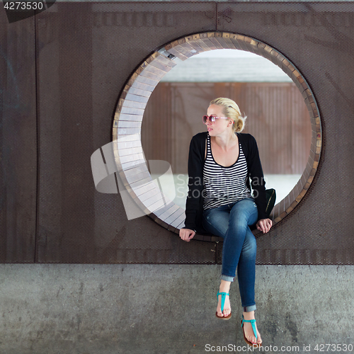 Image of Young thoughtful woman relaxing on bench in city park.