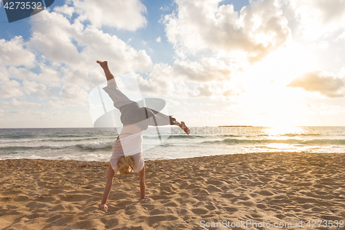 Image of Free Happy Woman Turning Cartwheel Enjoying Sunset on Sandy Beach.