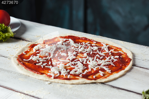 Image of Closeup of a home made raw pizza with cheese and tomato sauce on a wooden background