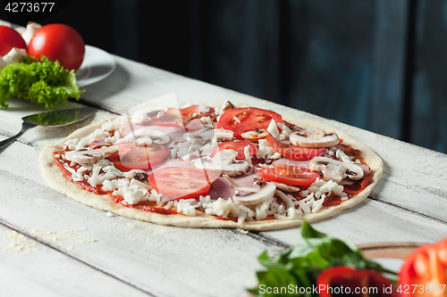 Image of Closeup of a home made raw pizza with cheese and tomato sauce on a wooden background