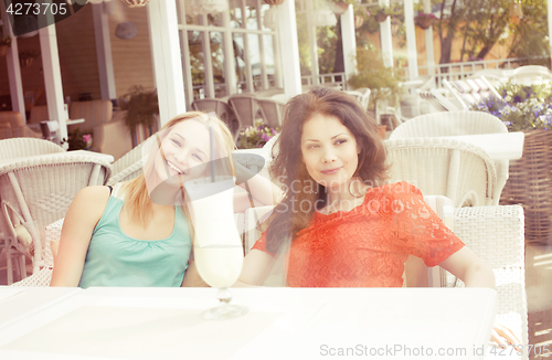 Image of portrait of two pretty modern real girl friends in cafe open air interior drinking and talking, having chat and coctail, lifestyle friendship concept