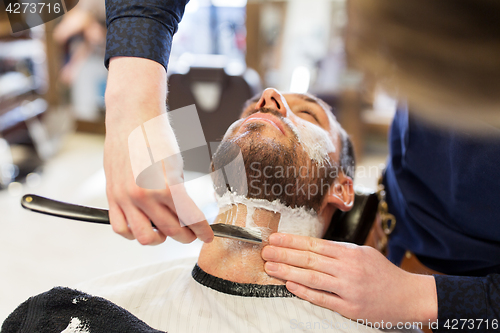 Image of man and barber with straight razor shaving beard