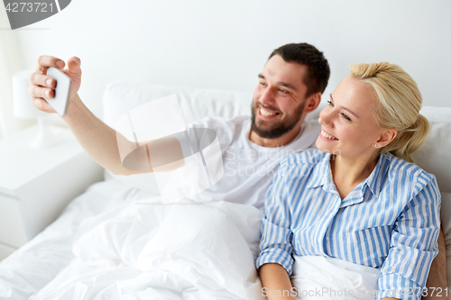 Image of happy couple with smartphone taking selfie at home