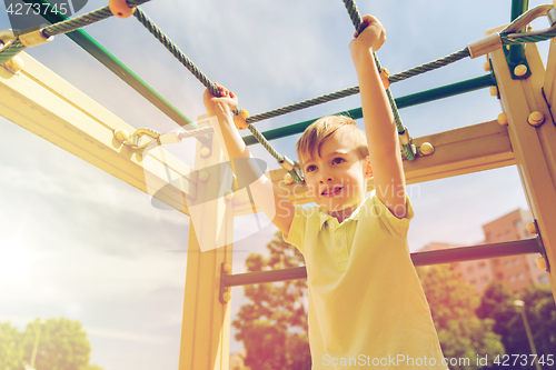 Image of happy little boy climbing on children playground