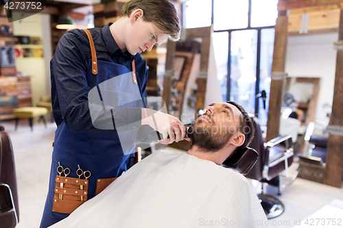 Image of man and barber with trimmer cutting beard at salon