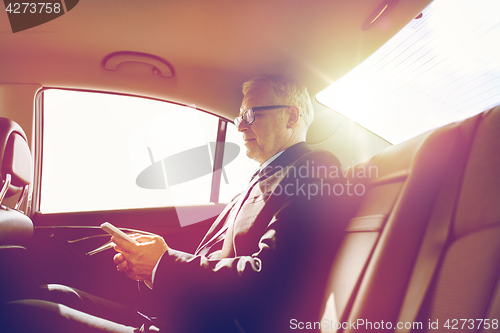 Image of senior businessman texting on smartphone in car