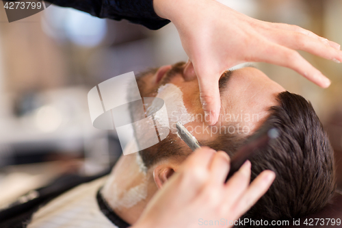 Image of man and barber with straight razor shaving beard