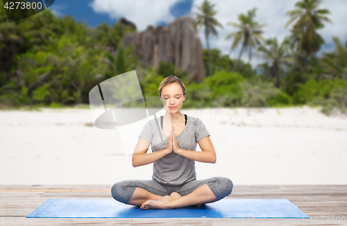 Image of woman doing yoga meditation in lotus pose on beach