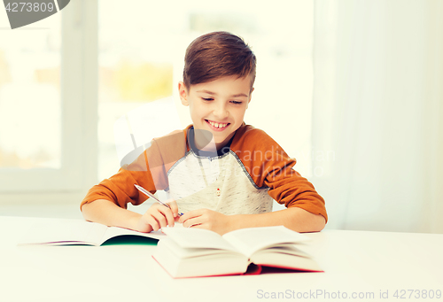 Image of smiling student boy writing to notebook at home