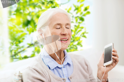 Image of senior woman with smartphone and earphones at home