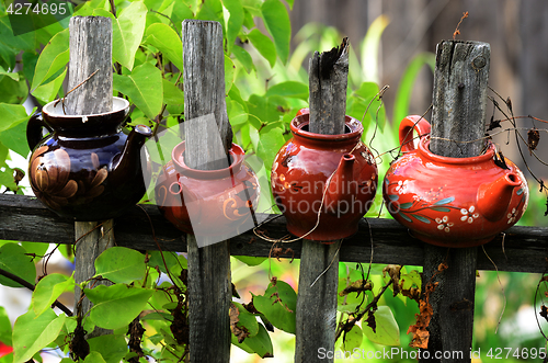 Image of four ceramic teapots on a wooden fence