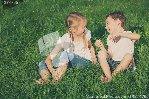 Image of Two happy children playing near the tree on the grass at the day