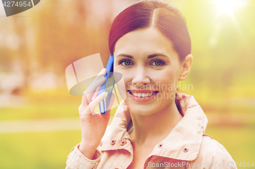 Image of smiling woman calling on smartphone in park