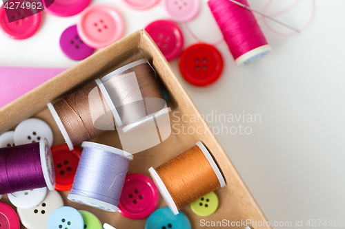 Image of box with thread spools and sewing buttons on table