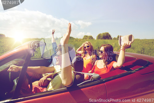 Image of happy friends driving in cabriolet car at country