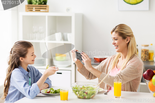 Image of woman photographing daughter by smartphone at home