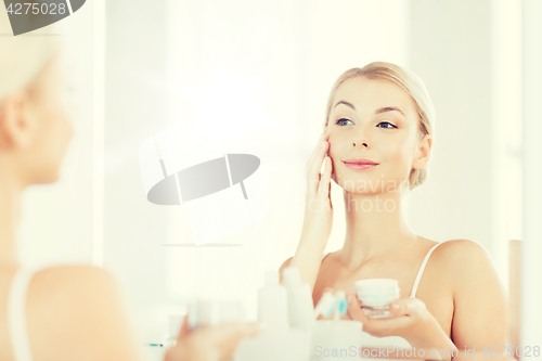 Image of happy woman applying cream to face at bathroom