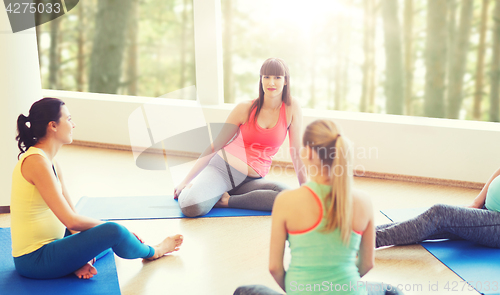 Image of happy pregnant women sitting on mats in gym