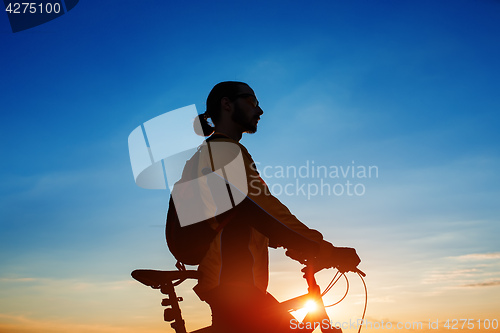 Image of Silhouette of cyclist and a bike on sky background