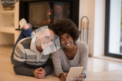 Image of multiethnic couple using tablet computer on the floor