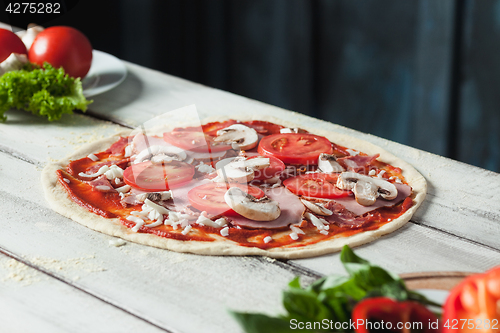 Image of Closeup of a home made raw pizza with cheese and tomato sauce on a wooden background