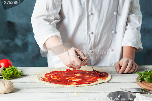 Image of Closeup hand of chef baker in white uniform making pizza at kitchen