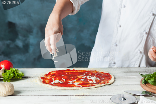 Image of Closeup hand of chef baker in white uniform making pizza at kitchen