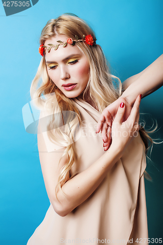 Image of young pretty blond girl with curly blond hair and little lowers happy smiling on blue sky background, lifestyle people concept