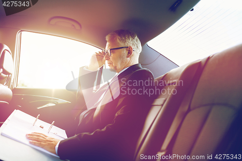 Image of senior businessman with papers driving in car