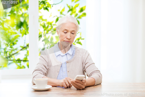 Image of senior woman with smartphone texting at home