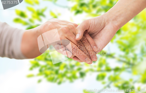 Image of close up of senior and young woman holding hands