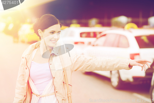 Image of smiling young woman waving hand and catching taxi