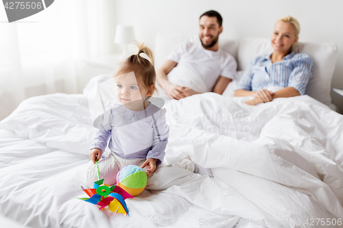 Image of happy child with toys and parents in bed at home