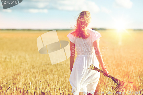 Image of young woman with cereal spikelets walking on field