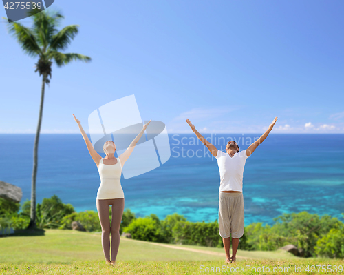 Image of happy couple making yoga exercises on beach