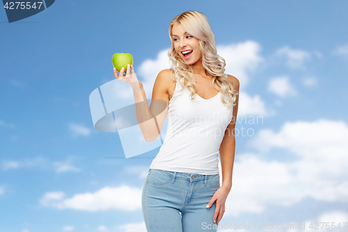 Image of happy young woman with green apple over blue sky
