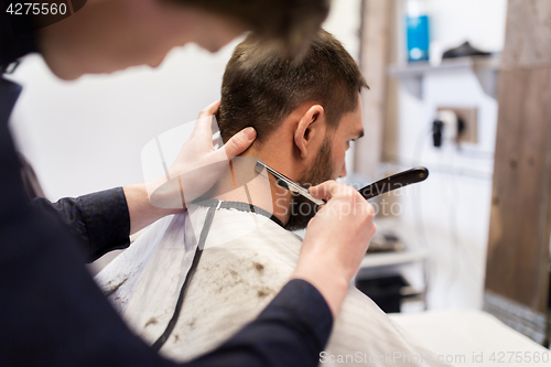 Image of man and barber with straight razor shaving hair