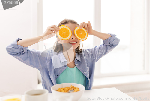 Image of happy girl with orange having breakfast at home