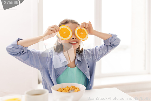 Image of happy girl with orange having breakfast at home