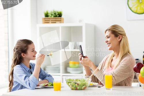 Image of woman photographing daughter by smartphone at home