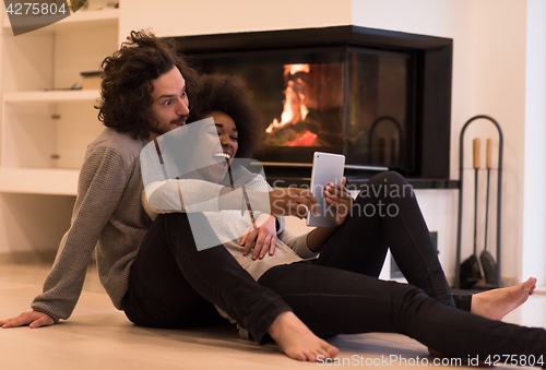 Image of multiethnic couple using tablet computer on the floor