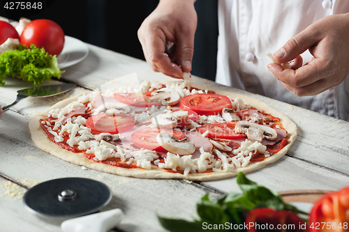 Image of Closeup hand of chef baker in white uniform making pizza at kitchen