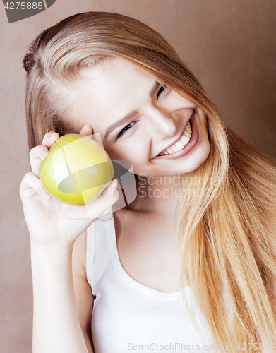 Image of young pretty blond woman with green apple happy cheerful smiling close up on warm brown background, lifestyle real people concept