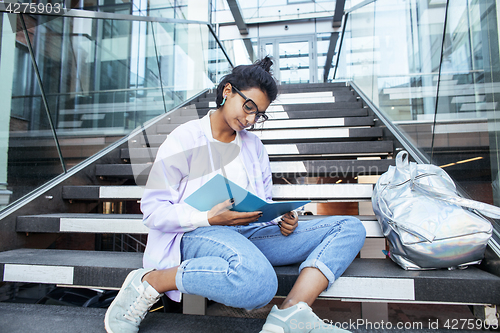 Image of young cute indian girl at university building sitting on stairs reading a book, wearing hipster glasses, lifestyle people concept
