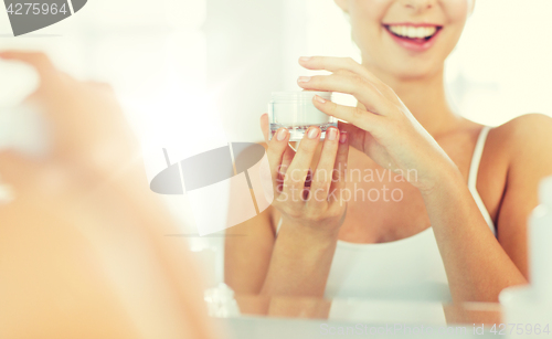 Image of happy woman with face cream at bathroom