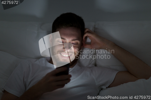 Image of happy young man with smartphone in bed at night