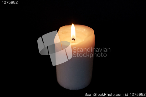 Image of candle burning in darkness over black background