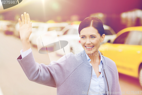 Image of smiling young woman with waving hand over taxi